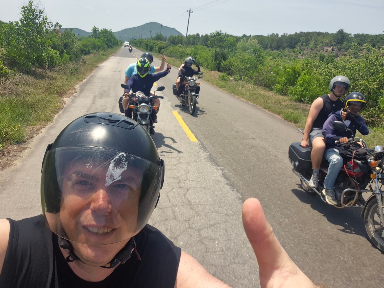 Helmet selfie of a guest with the riding group strung out along a country road behind