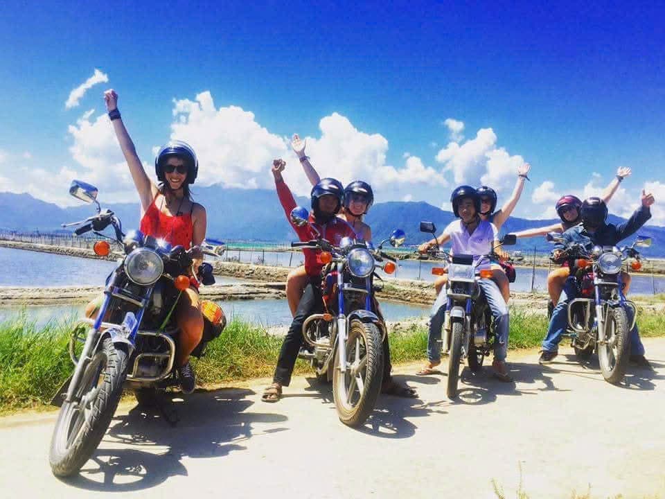 Riders and guides with arms raised on bikes beside the lagoon under blue sky